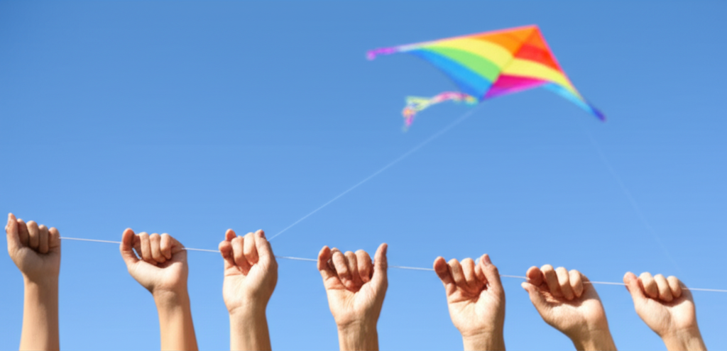 A close-up shot of multiple hands, spanning different ages from child to elderly, all holding onto a single, brightly colored kite string, with the kite soaring high in a clear blue sky in the background. The hands are touching or overlapping, subtly showing warmth and connection.