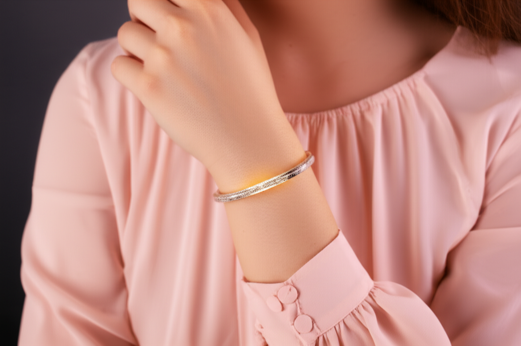A close-up shot of a woman's wrist adorned with a delicate, intricately designed bracelet that subtly glows with a soft, internal light. The bracelet's design is elegant and minimalist, appearing more like a piece of jewelry than a tech gadget. The woman is wearing a flowing, modestly cut sleeve in a pastel color, partially obscuring the bracelet but highlighting its subtle light and elegant form.